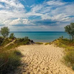 Ścieżka przez piaszczyste wydmy prowadzi do turkusowego jeziora. To idealne miejsce na relaks, jak na plaży nad Jeziorem Rożnowskim.