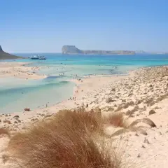 Piękne chania plaże z turkusową wodą, łagodnymi falami i piaszczystym wybrzeżem. W oddali widać statki wycieczkowe.