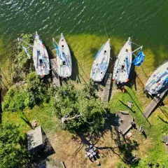 Mazury atrakcje wodne: białe żaglówki cumują przy brzegu, zielona trawa i drzewa tworzą malowniczy krajobraz.