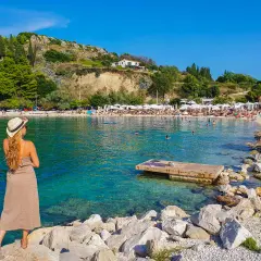 Kobieta w kapeluszu podziwia słoneczne plaże w Splicie. Woda jest krystalicznie czysta, a na brzegu widać wielu turystów.