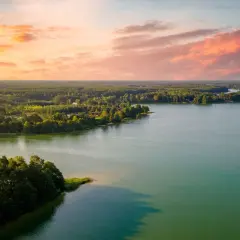 Zachód słońca nad jeziorem, z lasem i domkami w tle. Idealne, fajne miejsca nad jeziorem na relaks.