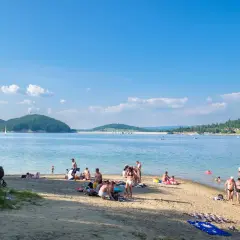 Polańczyk atrakcje: plażowicze odpoczywają nad Soliną, w tle żaglówka i zielone wzgórza.