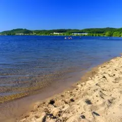 Słoneczny dzień nad zalewem Sulejowskim. Piaszczysta plaża, błękitna woda i zielone wzgórza w tle.