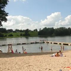 Letnie popołudnie na piaszczystej plaży nad jeziorem. Ludzie odpoczywają, kąpią się, a dzieci bawią się w wodzie. To typowy widok dla mazurskich miejscowości.