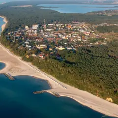 Jarosławiec: widok z lotu ptaka na plażę z falochronami, las i zabudowania.