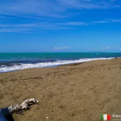 Spokojna plaża nudystów z turkusową wodą i piaszczystym brzegiem.