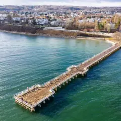 Spacer w Sopocie, najdłuższe molo w Polsce, wchodzi w turkusowe morze. W tle widać zabudowania i wzgórza.