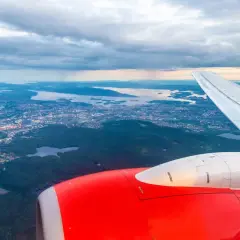 Widok z samolotu na Oslo Torp i okoliczne fiordy. Czerwony silnik i białe skrzydło samolotu na pierwszym planie.