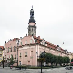 Różowy ratusz z wieżą zegarową to główna z bolesławiec atrakcje. Na rynku widać też kamienice i kawiarniane stoliki.