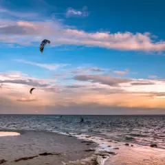 Zachód słońca nad Bałtykiem. Kilku śmiałków uprawia kitesurfing w Polsce, unosząc się na falach pod kolorowym niebem.
