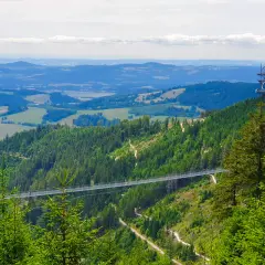Widok na najdłuższy most Czech, zawieszony nad zieloną doliną. W oddali widać wieżę widokową.
