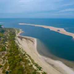 Piaskowa mierzeja na zachodnim wybrzeżu Bałtyku, otoczona zielenią i wodą, tworzy malowniczy krajobraz.
