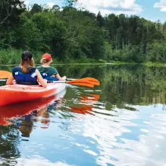 Dwie osoby płyną kajakiem po spokojnej rzece, ciesząc się pięknem przyrody. To idealny spływ kajakowy Mazury.