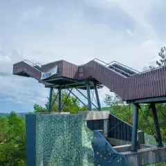 Drewniana konstrukcja widokowa na górze Markowca w Rumi, z widocznymi schodami i balustradami, otoczona zielenią drzew.