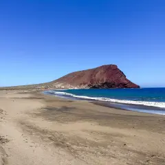 Pusta plaża na Teneryfie z charakterystyczną czerwoną górą w tle i turkusowym oceanem. Idealne miejsce na relaks.