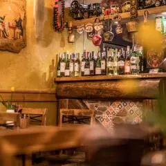 Drewniane stoły i krzesła w przytulnych restauracjach w Szklarskiej Porębie. Na półce rząd butelek wina, a nad nimi ozdoby.