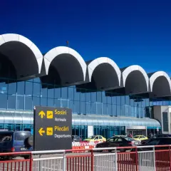 Nowoczesny terminal lotniska w Bukareszcie z charakterystycznymi łukami dachu. Tablice kierują do przylotów i odlotów.