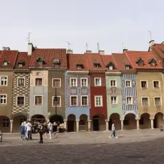 Kolorowe kamieniczki na poznańskim rynku, z arkadami i ludźmi spacerującymi po bruku.