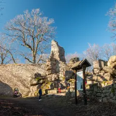 Ruiny zamku na Rudawach Janowickich, kamienne mury, skalne formacje i nagie drzewa pod błękitnym niebem.