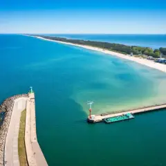 Molo we Władysławowie, z falochronem i latarnią morską, wita statki na tle piaszczystej plaży i turkusowego morza.