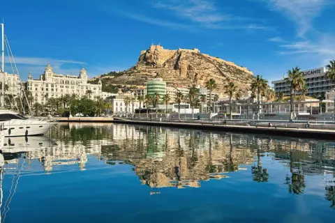 Widok na port i zamek Santa Barbara w Alicante. Luksusowe jachty odbijają się w spokojnej wodzie.