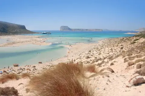 Piękne chania plaże z turkusową wodą, łagodnymi falami i piaszczystym wybrzeżem. W oddali widać statki wycieczkowe.