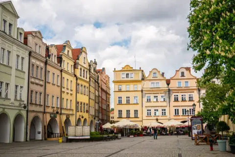Kolorowe kamienice na jeleniogórskim rynku, z arkadami i kawiarnianymi ogródkami, pod błękitnym niebem.