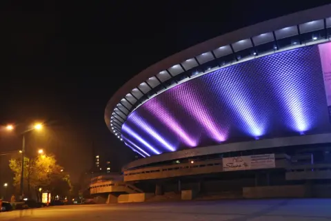 Nocne atrakcje w: Katowice. Spodek rozświetlony fioletowo-niebieskim światłem, nocą.