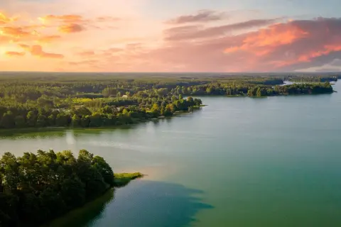 Zachód słońca nad jeziorem, z lasem i domkami w tle. Idealne, fajne miejsca nad jeziorem na relaks.