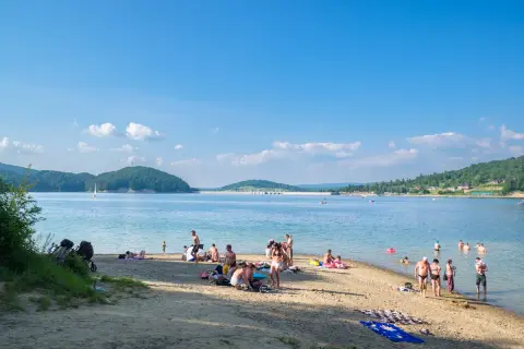Polańczyk atrakcje: plażowicze odpoczywają nad Soliną, w tle żaglówka i zielone wzgórza.