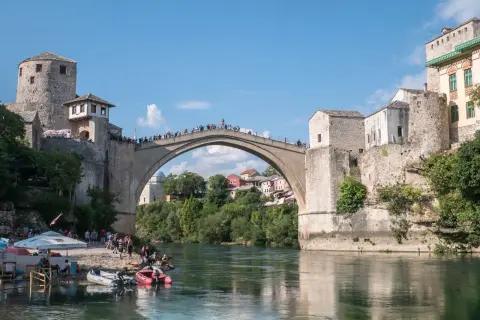 Mostar, Bośnia i Hercegowina: Słynny Stary Most z kamienia, tłumy ludzi na moście i brzegu, łodzie na rzece Neretwie.
