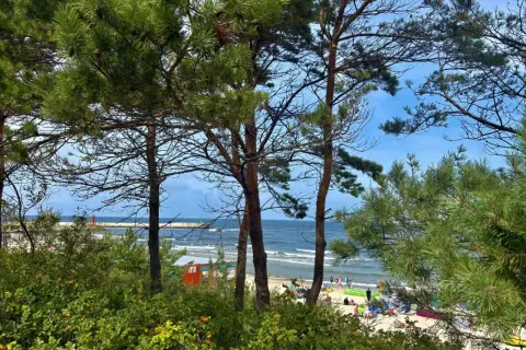 Widok na plażę w Mrzeżynie, z ludźmi odpoczywającymi na piasku i morzem w tle. To jedne z wielu mrzeżyno atrakcje.