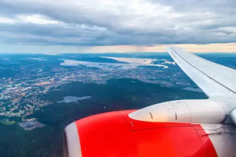 Widok z samolotu na Oslo Torp i okoliczne fiordy. Czerwony silnik i białe skrzydło samolotu na pierwszym planie.