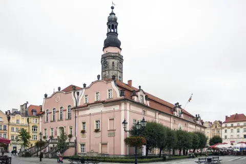 Różowy ratusz z wieżą zegarową to główna z bolesławiec atrakcje. Na rynku widać też kamienice i kawiarniane stoliki.