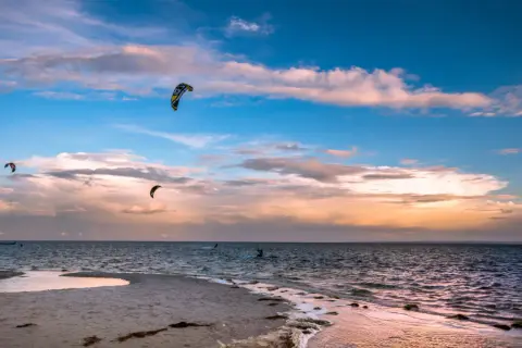 Zachód słońca nad Bałtykiem. Kilku śmiałków uprawia kitesurfing w Polsce, unosząc się na falach pod kolorowym niebem.