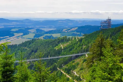 Widok na najdłuższy most Czech, zawieszony nad zieloną doliną. W oddali widać wieżę widokową.