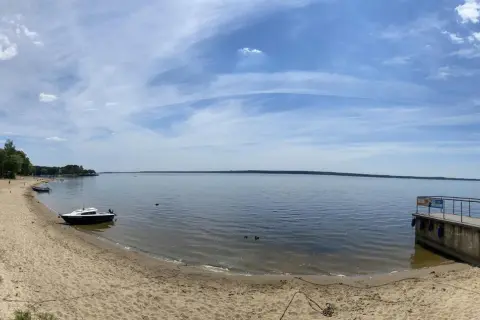 Piękny dzień nad jeziorami opolskimi. Piaszczysta plaża, spokojna woda i błękitne niebo zapraszają do wypoczynku.