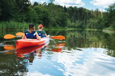 Dwie osoby płyną kajakiem po spokojnej rzece, ciesząc się pięknem przyrody. To idealny spływ kajakowy Mazury.