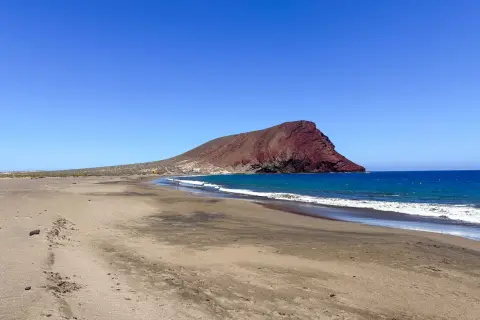 Pusta plaża na Teneryfie z charakterystyczną czerwoną górą w tle i turkusowym oceanem. Idealne miejsce na relaks.