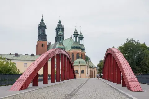 Czerwony most na poznańskiej trasie prowadzi do katedry. Spacerowicze podziwiają architekturę.