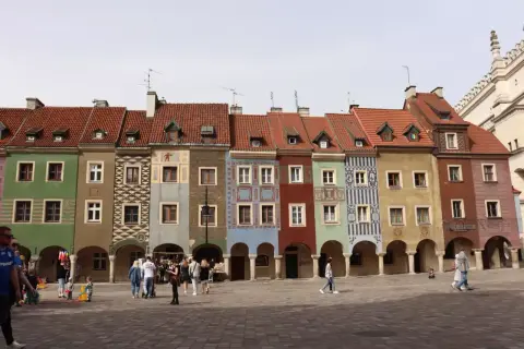 Kolorowe kamieniczki na poznańskim rynku, z arkadami i ludźmi spacerującymi po bruku.