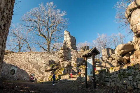 Ruiny zamku na Rudawach Janowickich, kamienne mury, skalne formacje i nagie drzewa pod błękitnym niebem.
