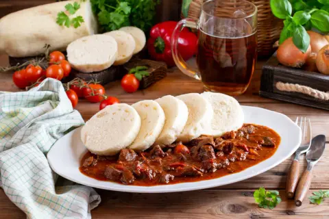 Gulasz z knedlikami, klasyka kuchni czeskiej, podany z piwem i świeżymi warzywami.