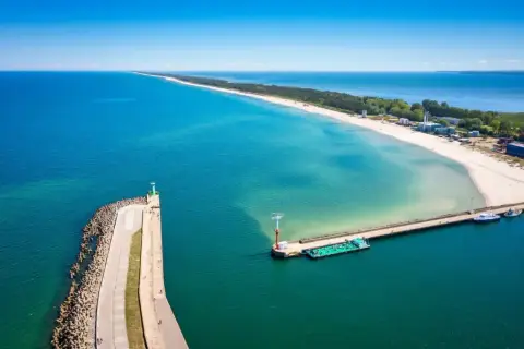 Molo we Władysławowie, z falochronem i latarnią morską, wita statki na tle piaszczystej plaży i turkusowego morza.