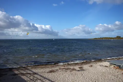 Plaża z piaskiem i morzem, na którym wielu kitesurferów korzysta z wiatru. Idealne miejsce, gdzie najcieplej nad morzem, by uprawiać sporty wodne.
