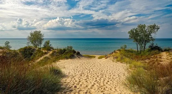 Ścieżka przez piaszczyste wydmy prowadzi do turkusowego jeziora. To idealne miejsce na relaks, jak na plaży nad Jeziorem Rożnowskim.