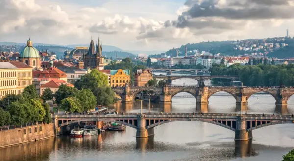 Widok na wiele mostów w Czechach, w tym Most Karola, nad Wełtawą, z praskim zamkiem i wzgórzami w tle.