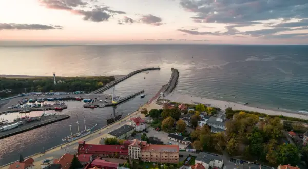 Widok z lotu ptaka na port i plażę w Ustce. Widać liczne łodzie, latarnię morską i falochrony. To idealne miejsce na odkrywanie ustka atrakcje.