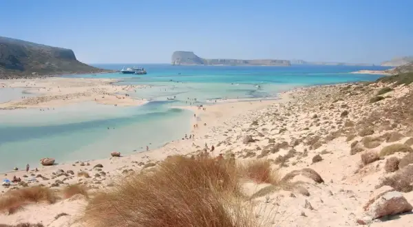 Piękne chania plaże z turkusową wodą, łagodnymi falami i piaszczystym wybrzeżem. W oddali widać statki wycieczkowe.