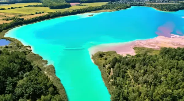 Turkusowe jezioro otoczone zielenią, przypominające polskie Malediwy. Piaskowe plaże i bujna roślinność tworzą malowniczy krajobraz.